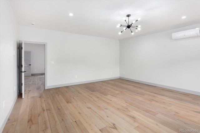 spare room featuring a chandelier, a wall mounted AC, and light hardwood / wood-style flooring