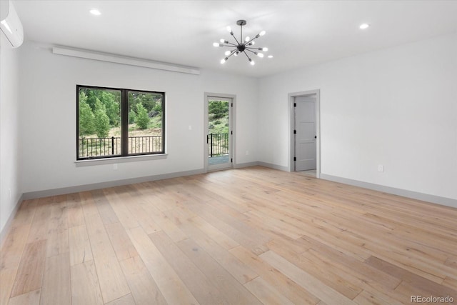 unfurnished room with an AC wall unit, a notable chandelier, and light hardwood / wood-style floors