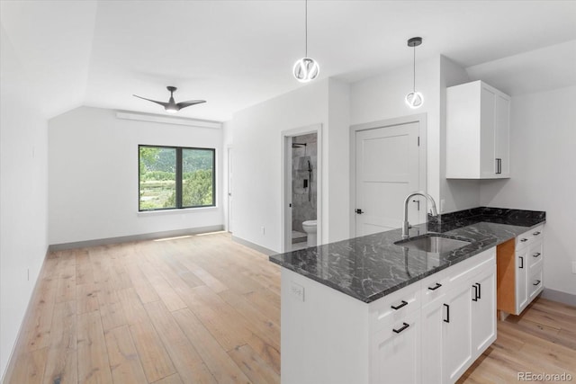 kitchen with sink, white cabinetry, decorative light fixtures, dark stone countertops, and light hardwood / wood-style floors