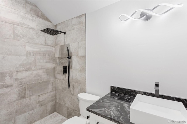 bathroom with lofted ceiling, vanity, toilet, and a tile shower