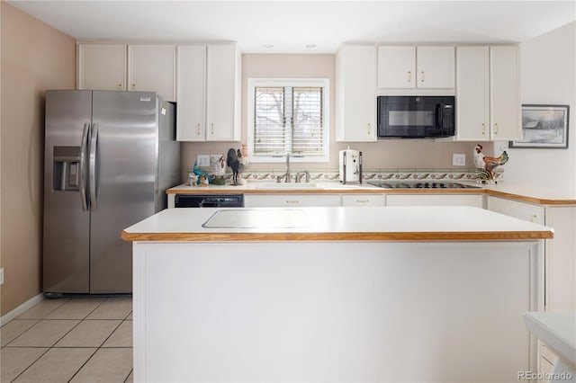 kitchen featuring light countertops, light tile patterned flooring, a sink, black microwave, and stainless steel fridge