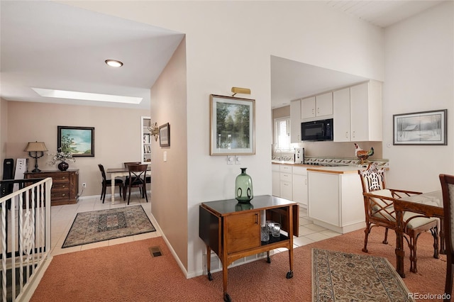 kitchen with visible vents, light tile patterned flooring, white cabinets, black microwave, and baseboards