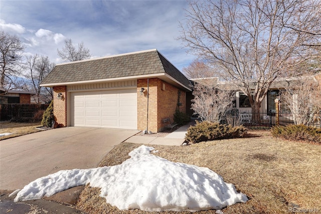 view of front of home featuring a garage, mansard roof, concrete driveway, fence, and brick siding