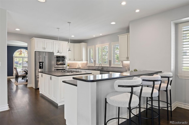 kitchen with stainless steel appliances, dark countertops, arched walkways, a center island, and plenty of natural light