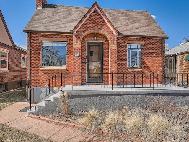 view of front of house with brick siding, roof with shingles, and a chimney