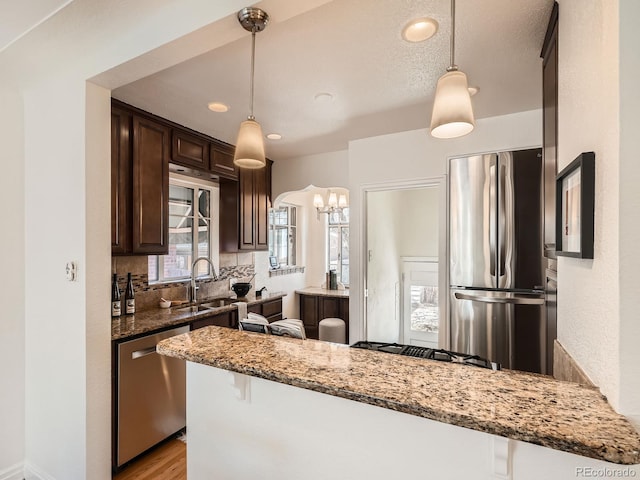 kitchen featuring dark brown cabinetry, decorative light fixtures, light stone countertops, stainless steel appliances, and a sink