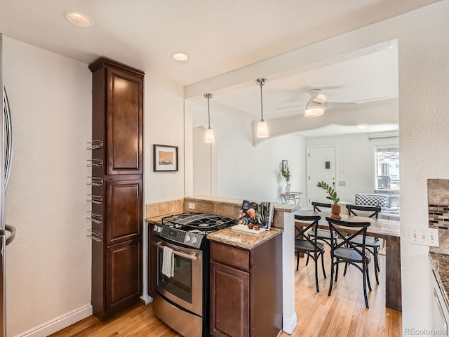 kitchen featuring light stone counters, light wood-style flooring, a ceiling fan, gas stove, and a peninsula