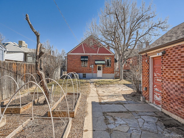 back of property featuring brick siding, a vegetable garden, and fence