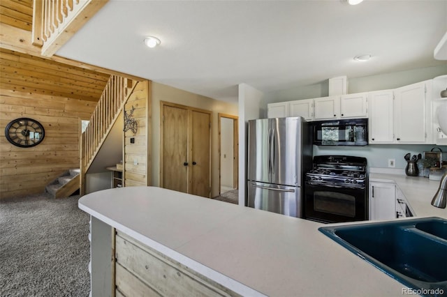 kitchen with wood walls, light countertops, carpet floors, white cabinets, and black appliances