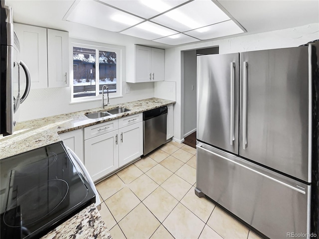 kitchen featuring light stone countertops, stainless steel appliances, sink, light tile patterned floors, and white cabinets