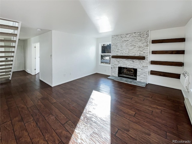 unfurnished living room with dark hardwood / wood-style floors, a stone fireplace, and an AC wall unit