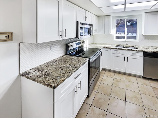 kitchen featuring appliances with stainless steel finishes, sink, stone counters, white cabinets, and light tile patterned flooring