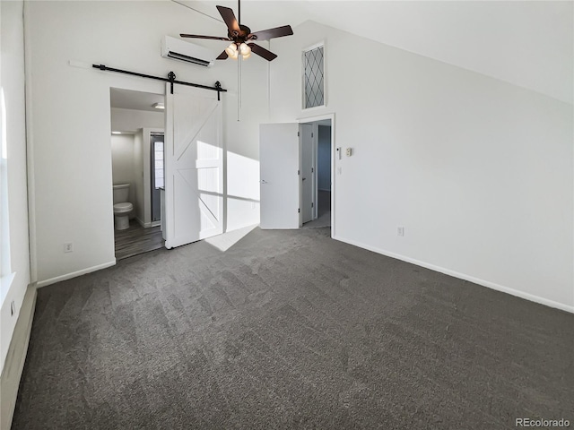 unfurnished bedroom with ensuite bath, a wall mounted AC, ceiling fan, dark colored carpet, and a barn door