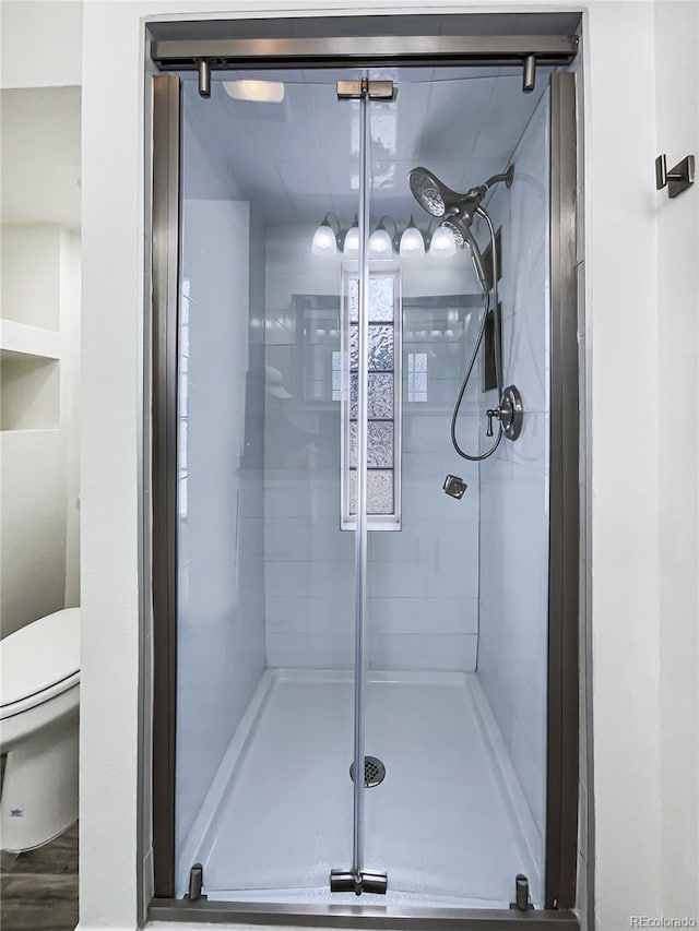 bathroom with toilet, an enclosed shower, and wood-type flooring