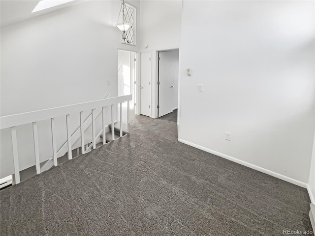 corridor featuring dark colored carpet, a high ceiling, and a skylight