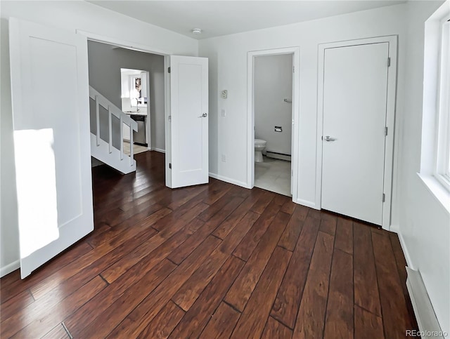 unfurnished bedroom featuring connected bathroom, dark wood-type flooring, and a baseboard heating unit