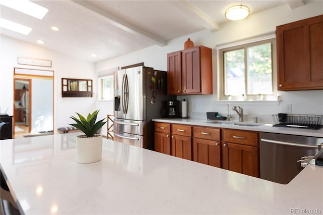 kitchen with a sink, stainless steel appliances, light stone countertops, and brown cabinets