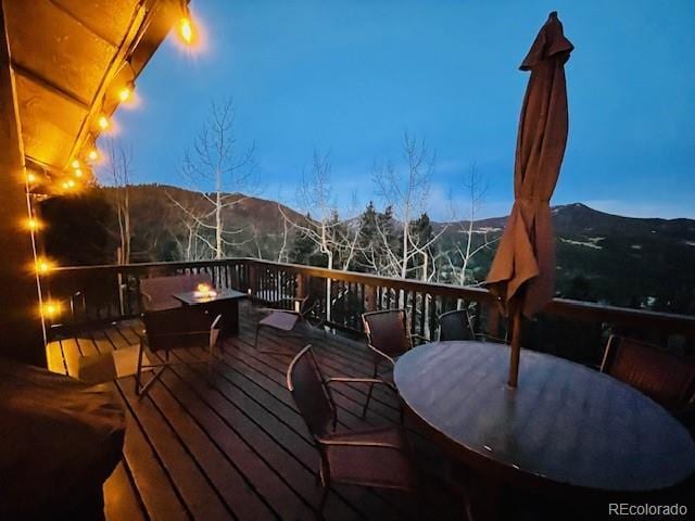 wooden terrace with outdoor dining space, a fire pit, and a mountain view