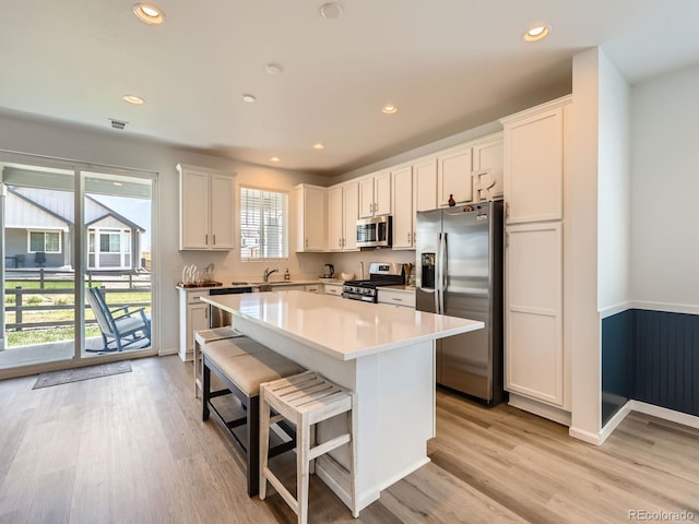 9054 Truckee Ct, Commerce City, CO 80022 - kitchen featuring appliances with stainless steel finishes, a kitchen island, light wood-type flooring, a breakfast bar, and white cabinets