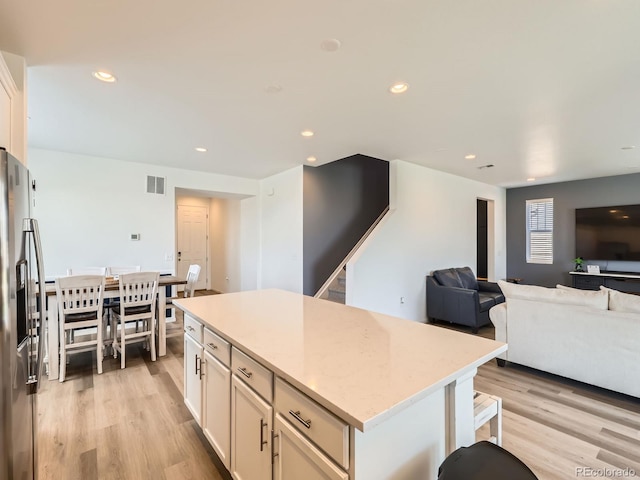 9054 Truckee Ct, Commerce City, CO 80022 - kitchen featuring stainless steel fridge, light wood-type flooring, a center island, open floor plan, and white cabinets