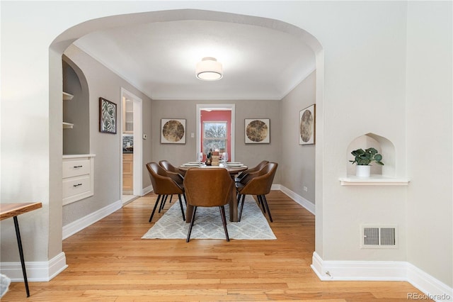 dining area with light wood-type flooring, crown molding, and built in features