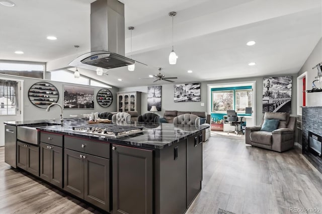 kitchen featuring vaulted ceiling with beams, island exhaust hood, stainless steel gas stovetop, open floor plan, and a sink