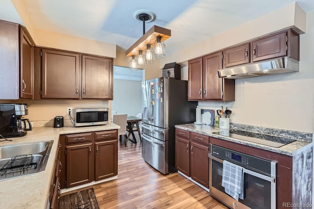 kitchen with sink, stainless steel appliances, light hardwood / wood-style floors, and decorative light fixtures