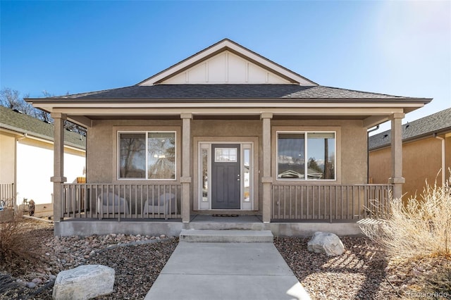 view of front of home with covered porch, board and batten siding, roof with shingles, and stucco siding