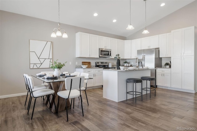 kitchen featuring a center island with sink, a kitchen breakfast bar, wood finished floors, stainless steel appliances, and white cabinets