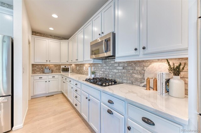 15389 W 50th Dr, Golden, CO 80403 - kitchen featuring appliances with stainless steel finishes, light stone counters, decorative backsplash, light wood finished floors, and white cabinets