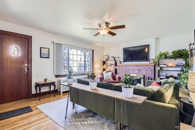 living room featuring a brick fireplace, ceiling fan, radiator heating unit, and light hardwood / wood-style flooring