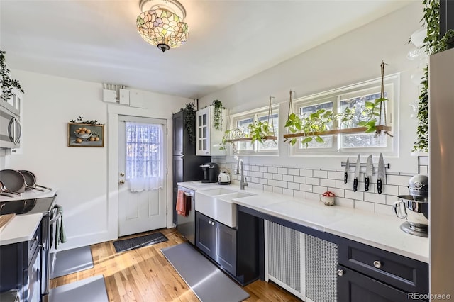 kitchen with decorative backsplash, light stone countertops, light wood-type flooring, stainless steel appliances, and sink