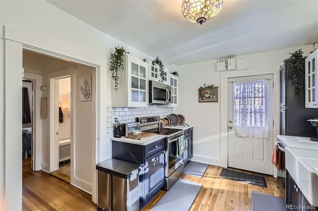 kitchen with tasteful backsplash, white cabinetry, light hardwood / wood-style flooring, and appliances with stainless steel finishes