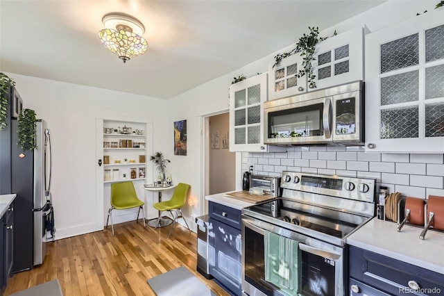 kitchen featuring white cabinets, blue cabinets, tasteful backsplash, light hardwood / wood-style floors, and stainless steel appliances