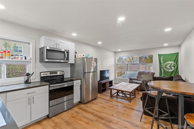 kitchen with white cabinetry, backsplash, stainless steel appliances, and light wood-type flooring