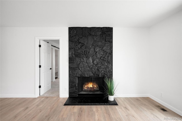 room details with a stone fireplace, wood finished floors, visible vents, and baseboards