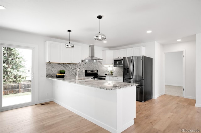 kitchen with wall chimney range hood, a sink, a peninsula, appliances with stainless steel finishes, and light stone countertops