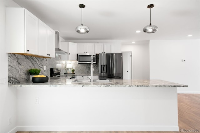 kitchen with stainless steel appliances, a peninsula, tasteful backsplash, white cabinetry, and wall chimney range hood