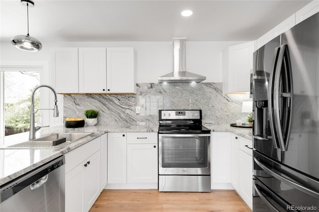 kitchen with white cabinets, stainless steel appliances, a sink, and wall chimney range hood