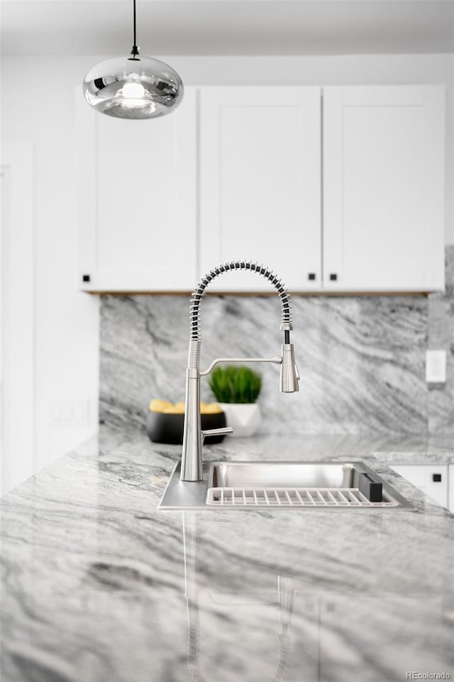 room details featuring decorative backsplash, white cabinetry, light stone countertops, and a sink