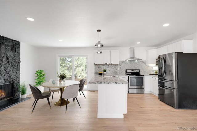 kitchen with stainless steel appliances, a sink, decorative backsplash, light stone counters, and wall chimney range hood