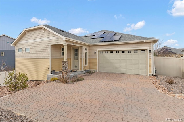 view of front of property featuring decorative driveway, fence, solar panels, and a garage
