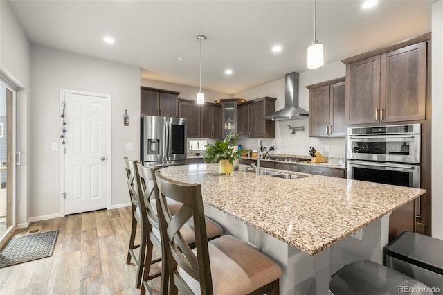 kitchen featuring wall chimney range hood, dark brown cabinets, light wood-type flooring, a sink, and recessed lighting