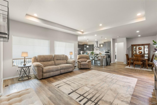 living room with a raised ceiling, light wood-style flooring, baseboards, and recessed lighting