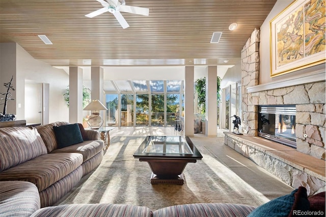 carpeted living room featuring a stone fireplace, ceiling fan, and wood ceiling