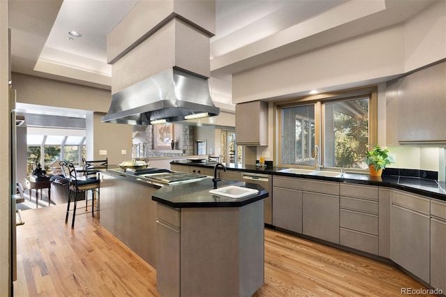 kitchen with sink, a tray ceiling, light hardwood / wood-style floors, kitchen peninsula, and island exhaust hood