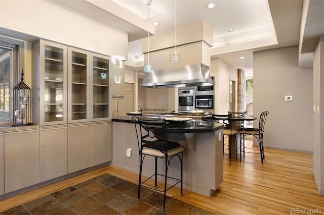 kitchen featuring a kitchen bar, kitchen peninsula, stainless steel oven, wall chimney range hood, and pendant lighting