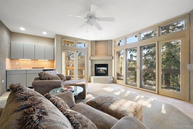 tiled living room featuring sink, a large fireplace, plenty of natural light, and ceiling fan