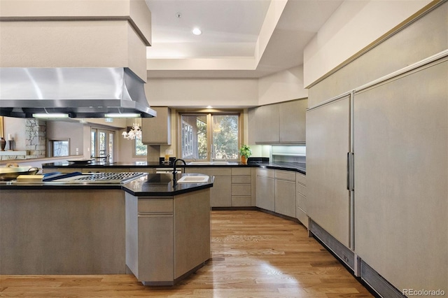 kitchen with light wood-type flooring, dark countertops, ventilation hood, and a sink