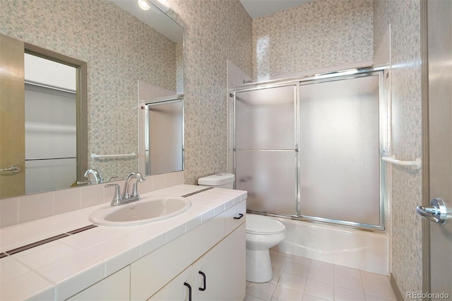 bathroom featuring bath / shower combo with glass door, toilet, vanity, tile patterned flooring, and wallpapered walls